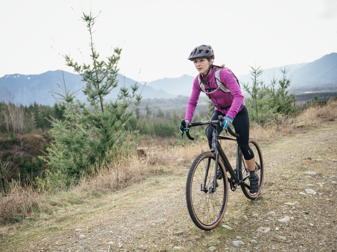 A person rides a gravel bike on a dirt path with mountains in the background