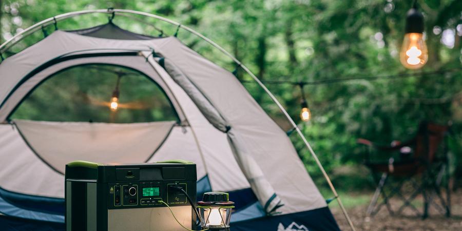 A portable power station is connected to a lantern at a campsite