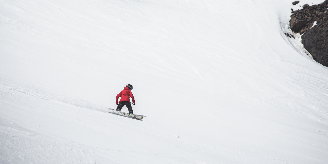 A person in red jacket snowboards down a slope