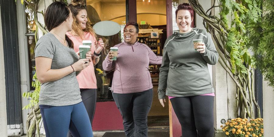 Four people dressed in athleisure wear laughing and holding coffees