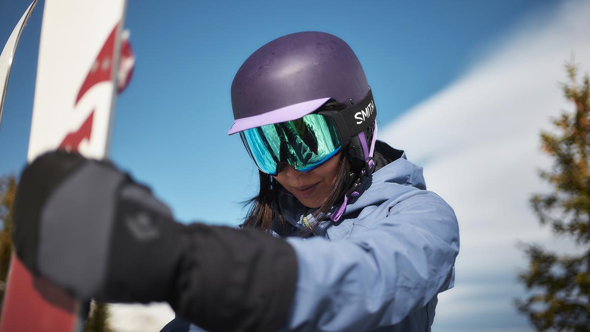 A person wearing snow goggles and a purple helmet looks down