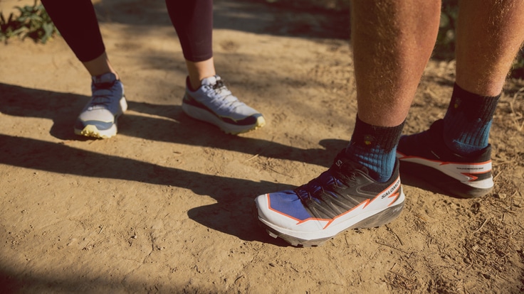 A from-the-leg-down image of a man and a woman each sporting the Salomon Thundercross trail-running shoes