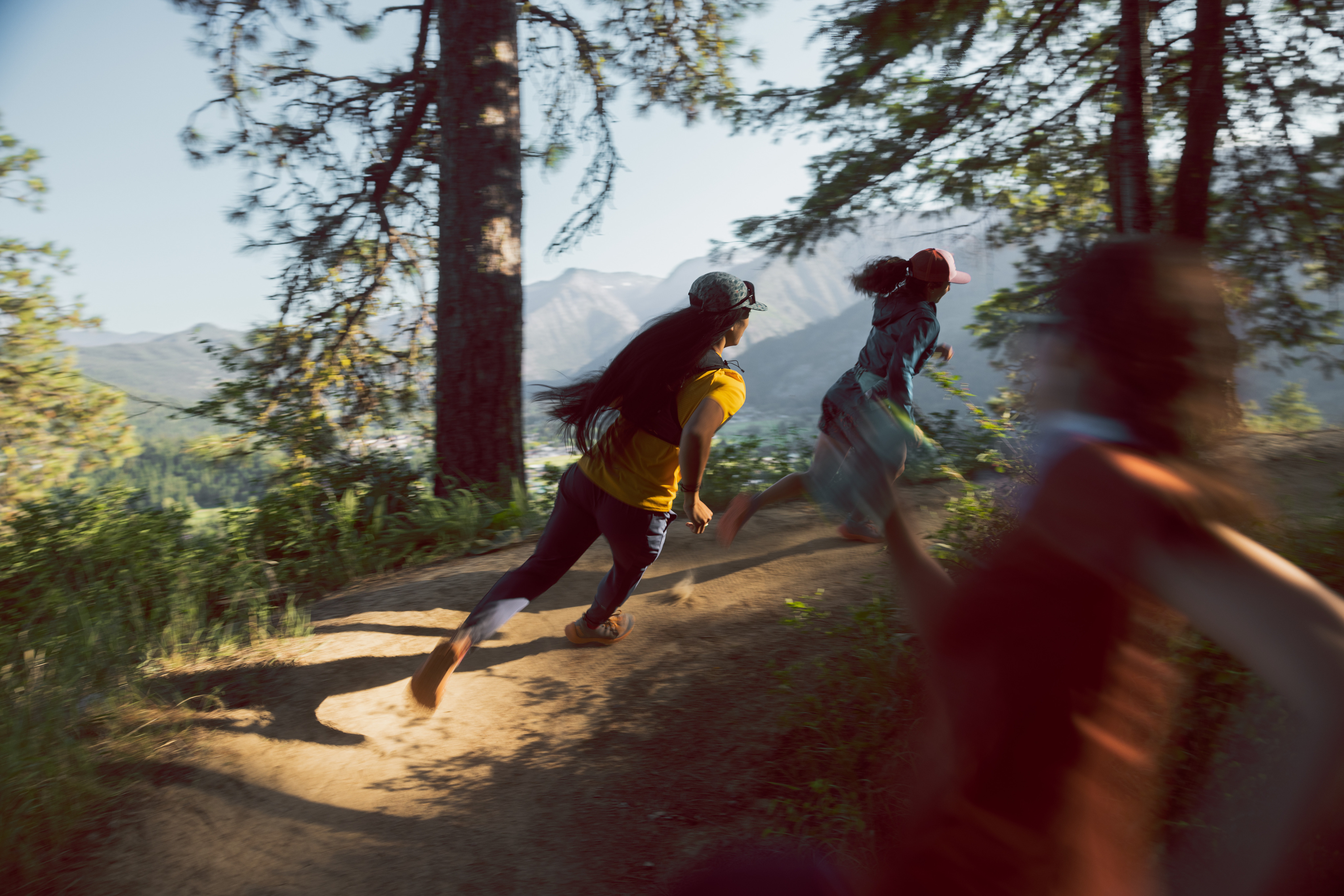 Three trail runners on a dirt path in the mountains.