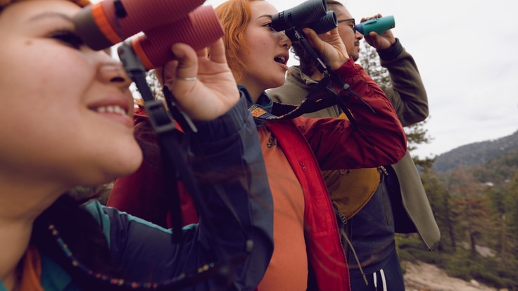 Three people looking through their Nocs Provisions binoculars, with the Nocs Provisions Woven Tapestry Strap