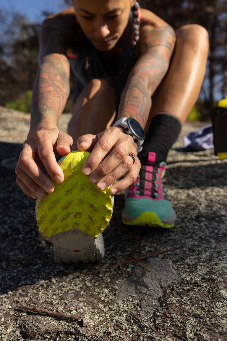 A person is sitting down and stretching their calf in the Salomon Sense Ride 5s, with the sole of the shoe facing the camera.