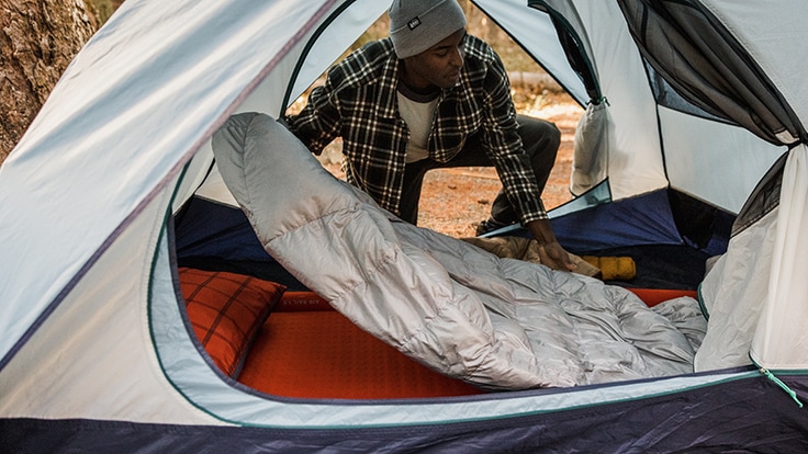 A camper unfurls an REI Magma sleeping bag in a tent.