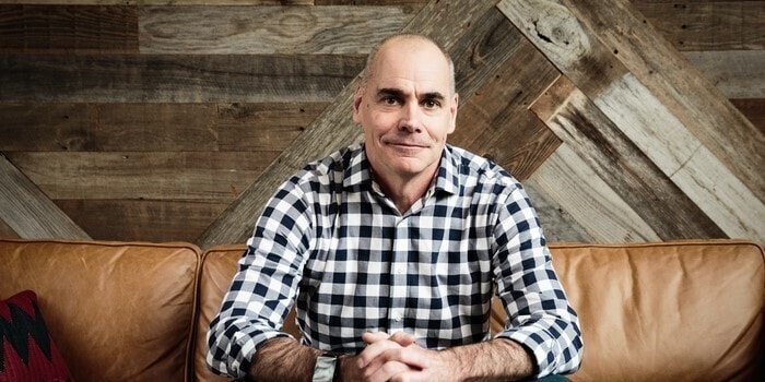 Chris Speyer, on a leather couch, in front of a patchwork wood wall