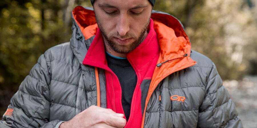 Man layers a fleece over his base layer and then zips up his top layer of a puffer jacket