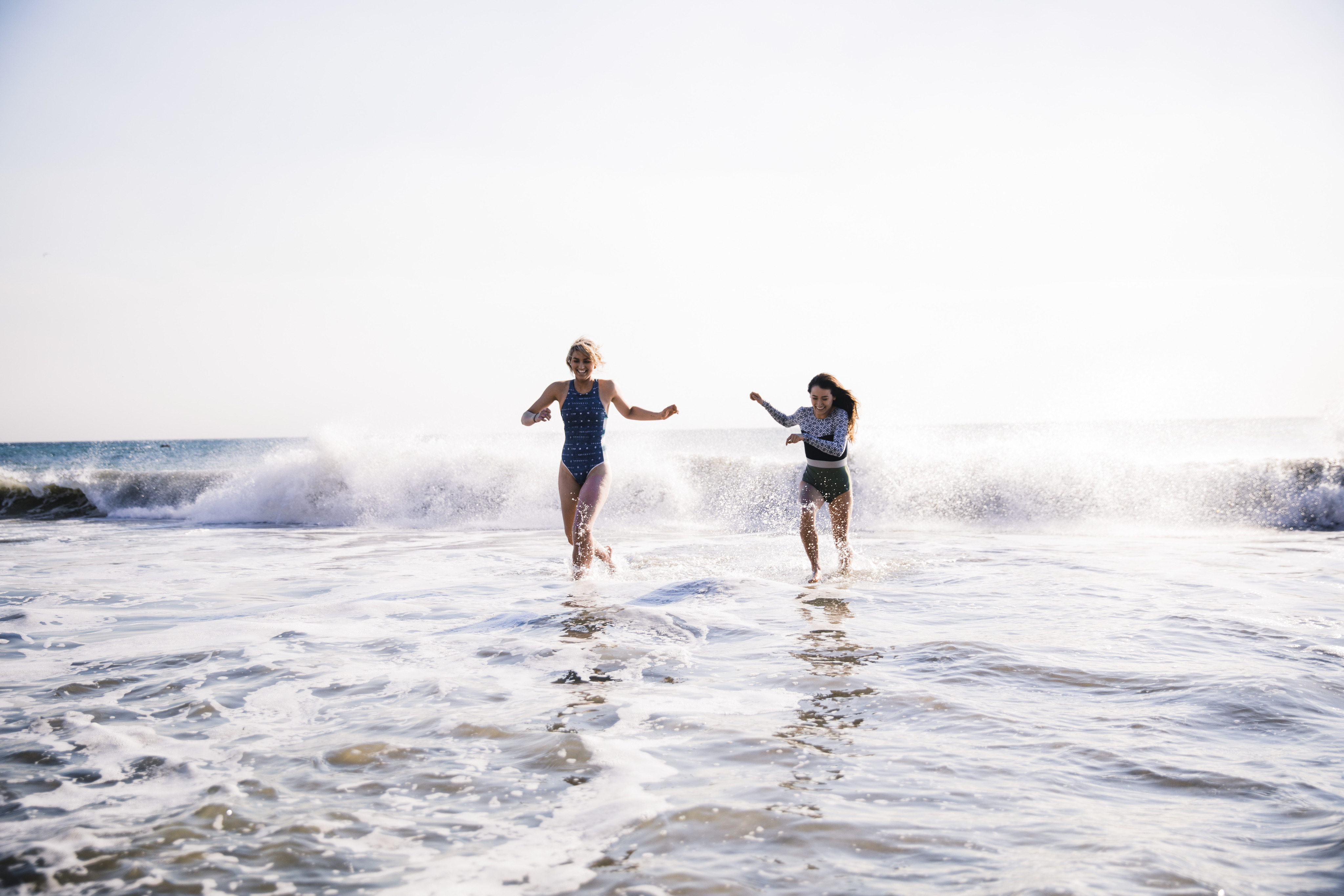 Two women wearing swimsuits are running out of the ocean water smiling