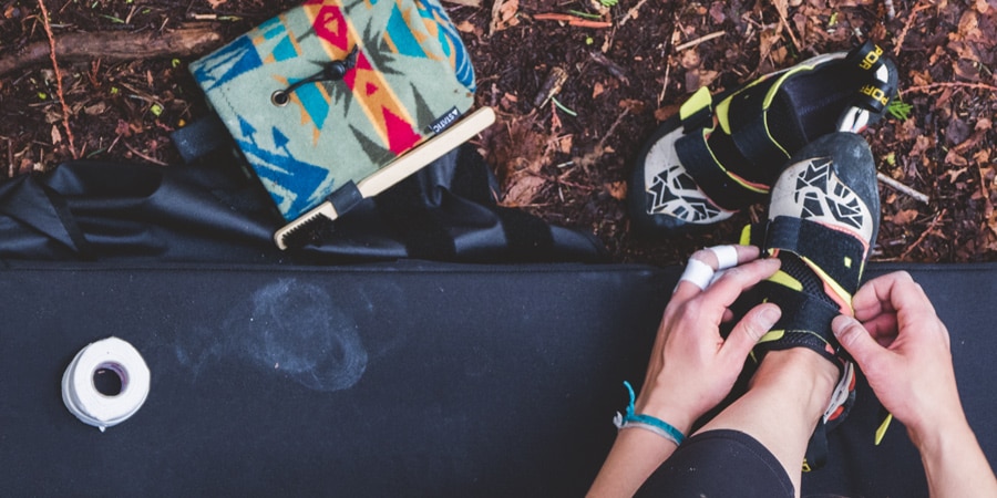 A climber with taped fingers puts on climbing shoes before bouldering