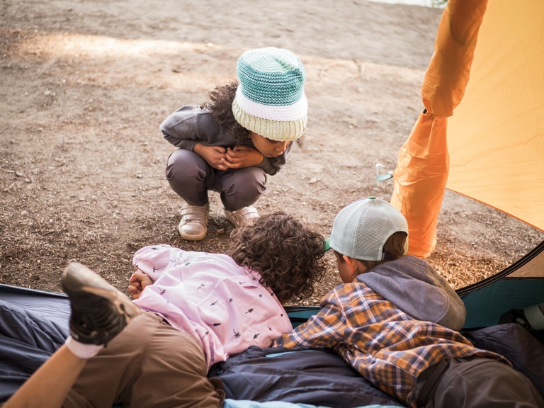 Three kids play in the dirt outside their tent.