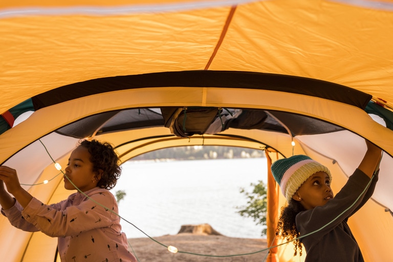 Two kids hang lights inside a tent.