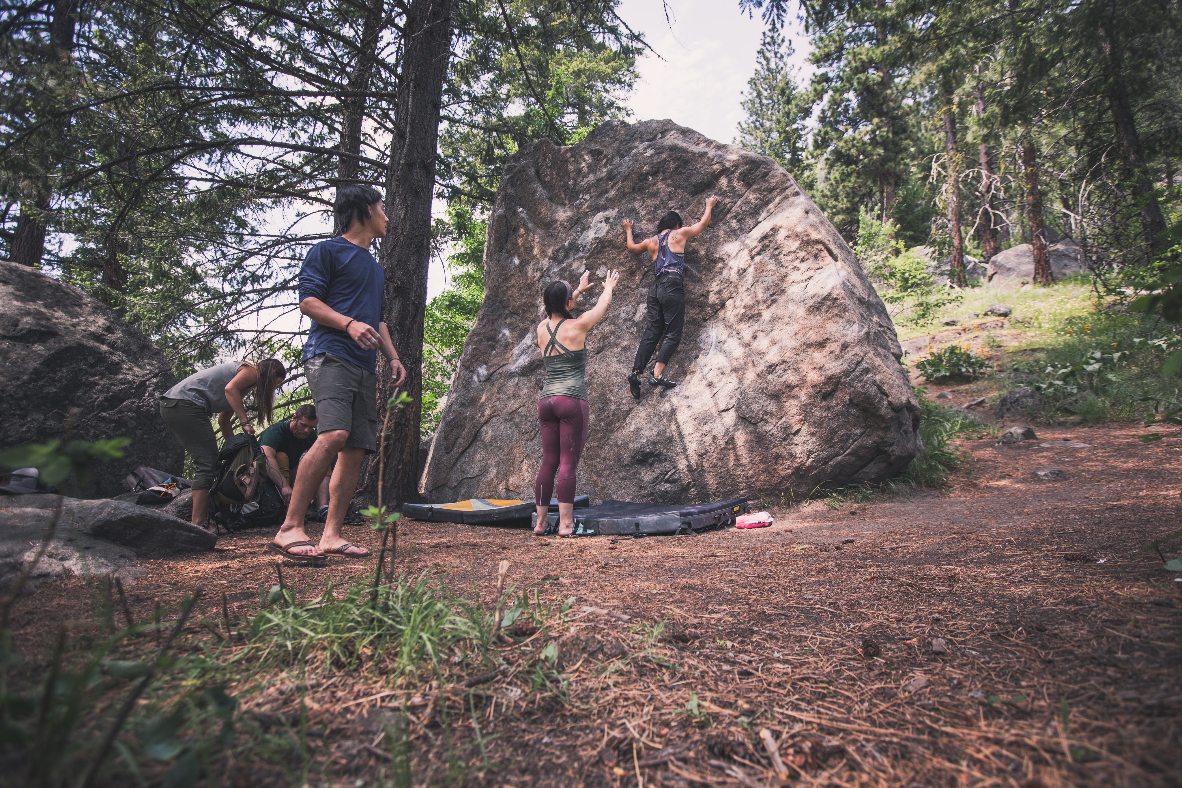 Climbing group gathers around a huge boulder supporting climber