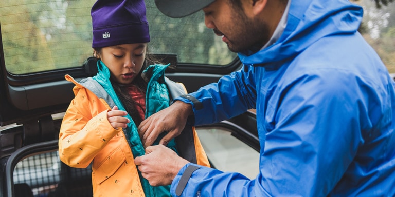 Man zips up a young girl's coat.