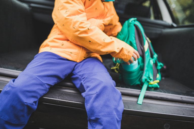 A kid sits in the back of a truck with a pack.