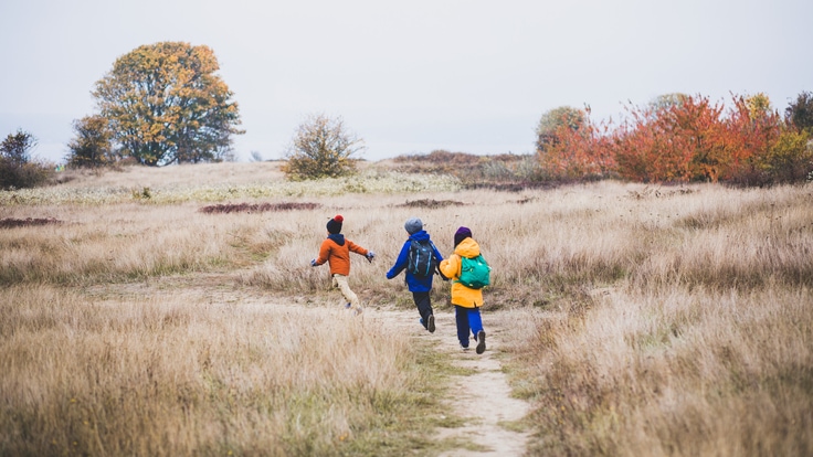 Three kids walk down a hiking trail.