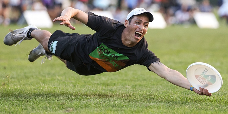 A competitive flying disc player leaps and dives to catch a disc