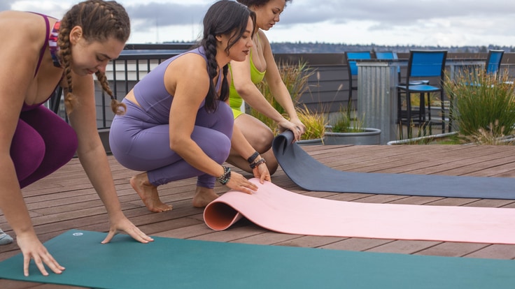 three women unrolling yoga mats outdoors