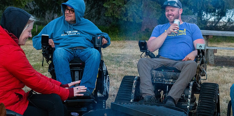 People using wheelchairs gathered around a campfire ring and laughing