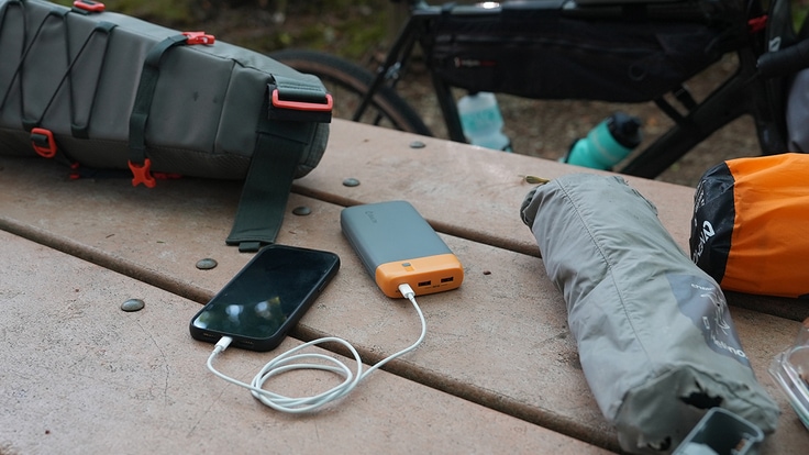 A portable power bank charges up a phone at a camp picnic table.