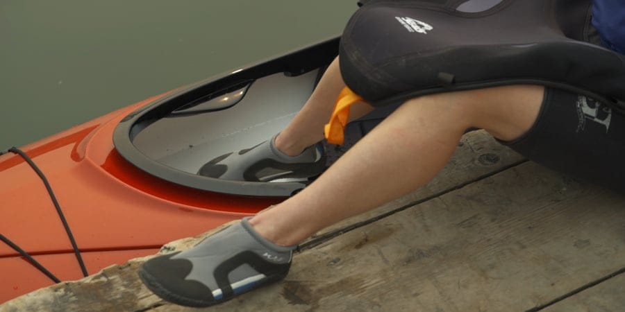 a kayaker starting to enter their kayak from a dock