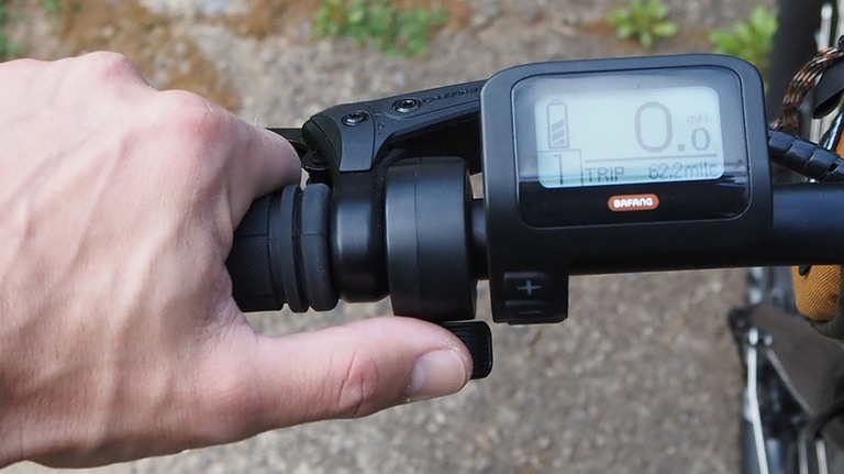 A person's thumb presses on the throttle lever on the handlebar of an electric bike