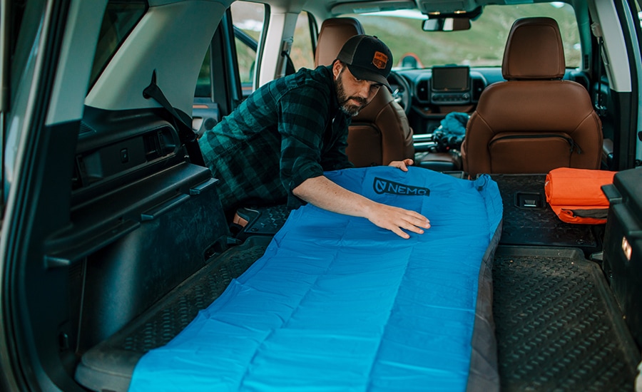 A person lays out their blue NEMO Quasar 3D Insulated Air Sleeping Pad in the back of their vehicle.