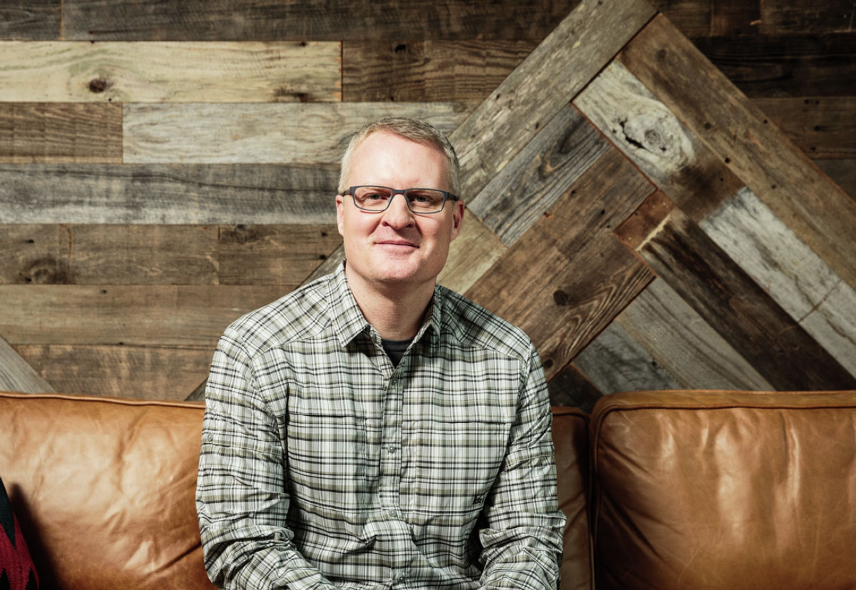 Eric Artz sitting in front of a wooden wall.