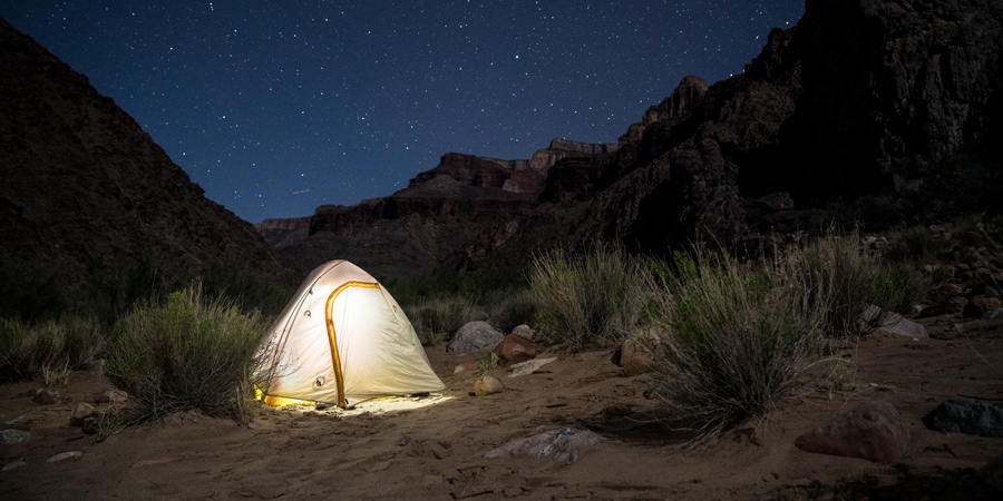 A backpacking tent glows against a starry sky