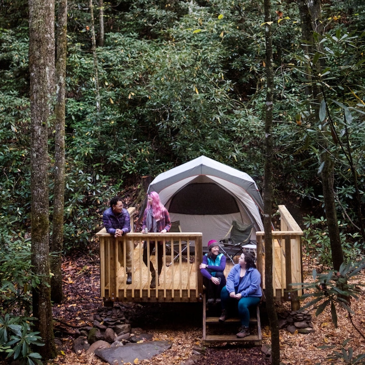 Four campers talk outside of a tent in the woods