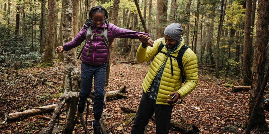 a dad helping his daughter walk along a downed tree