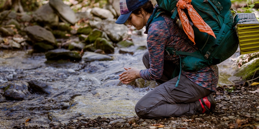 a backpacker washing their hands in a stream