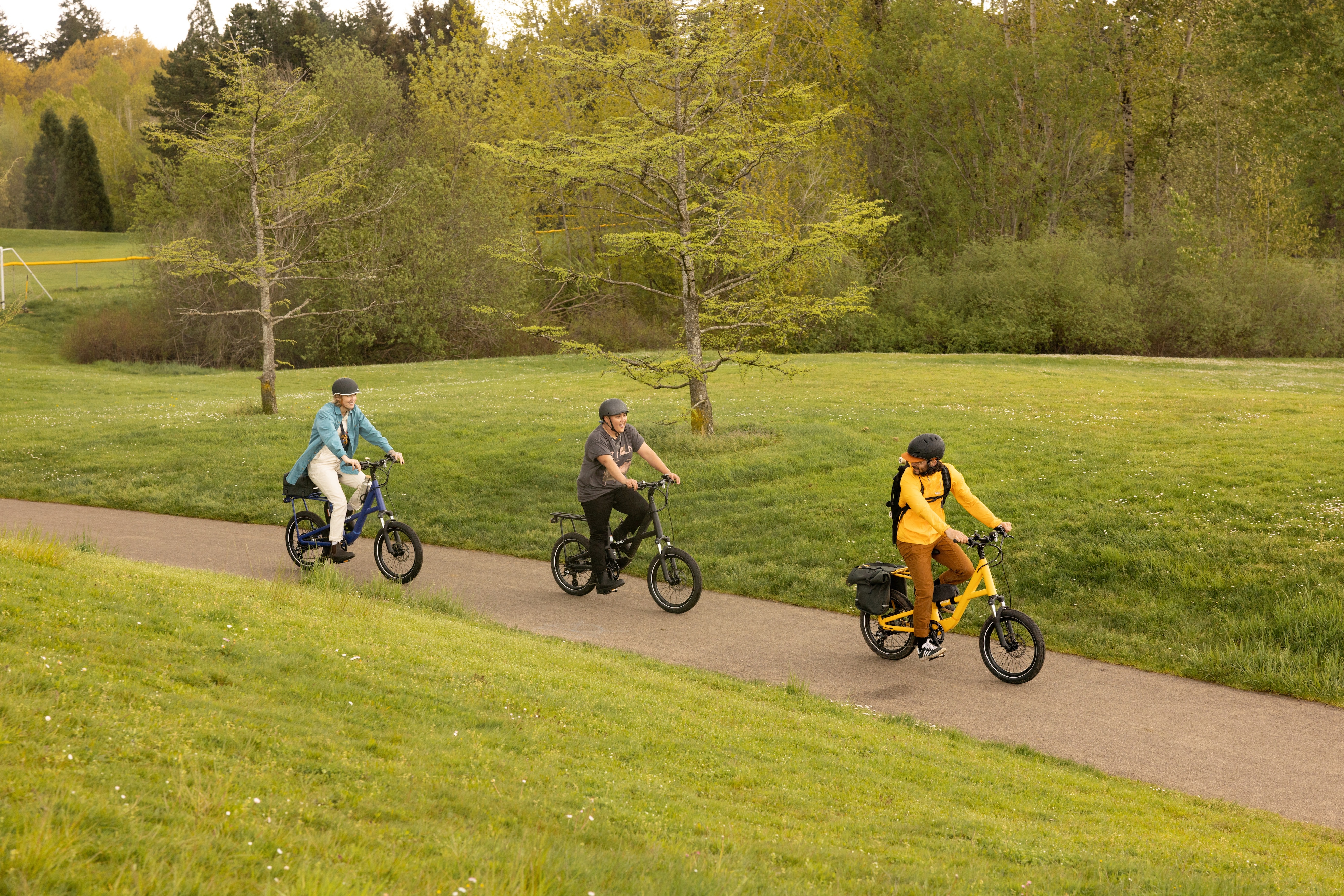 Three bicyclists ride e-bikes along a paved trail