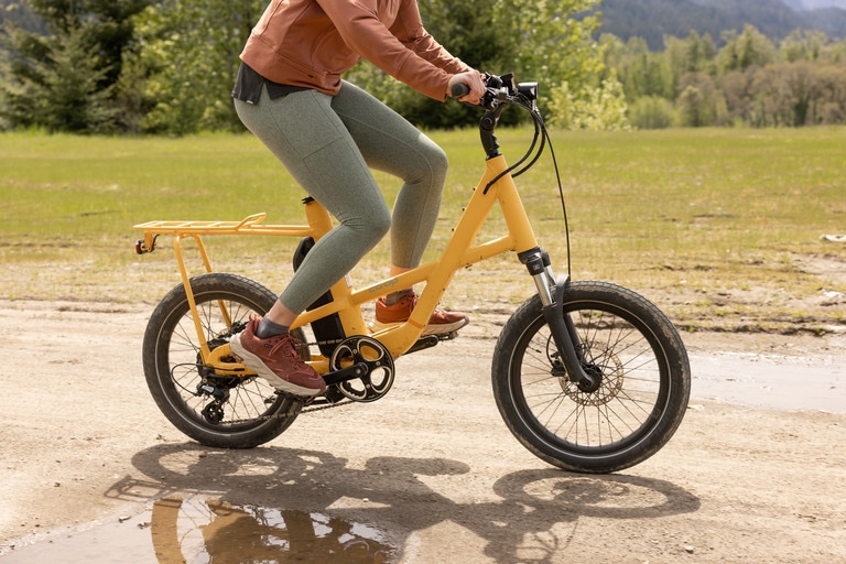 Person riding a yellow electric bike on a dirt path