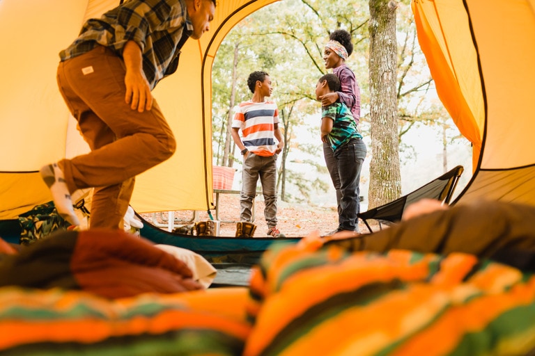 Two adults talk to two young boys outside a tent.