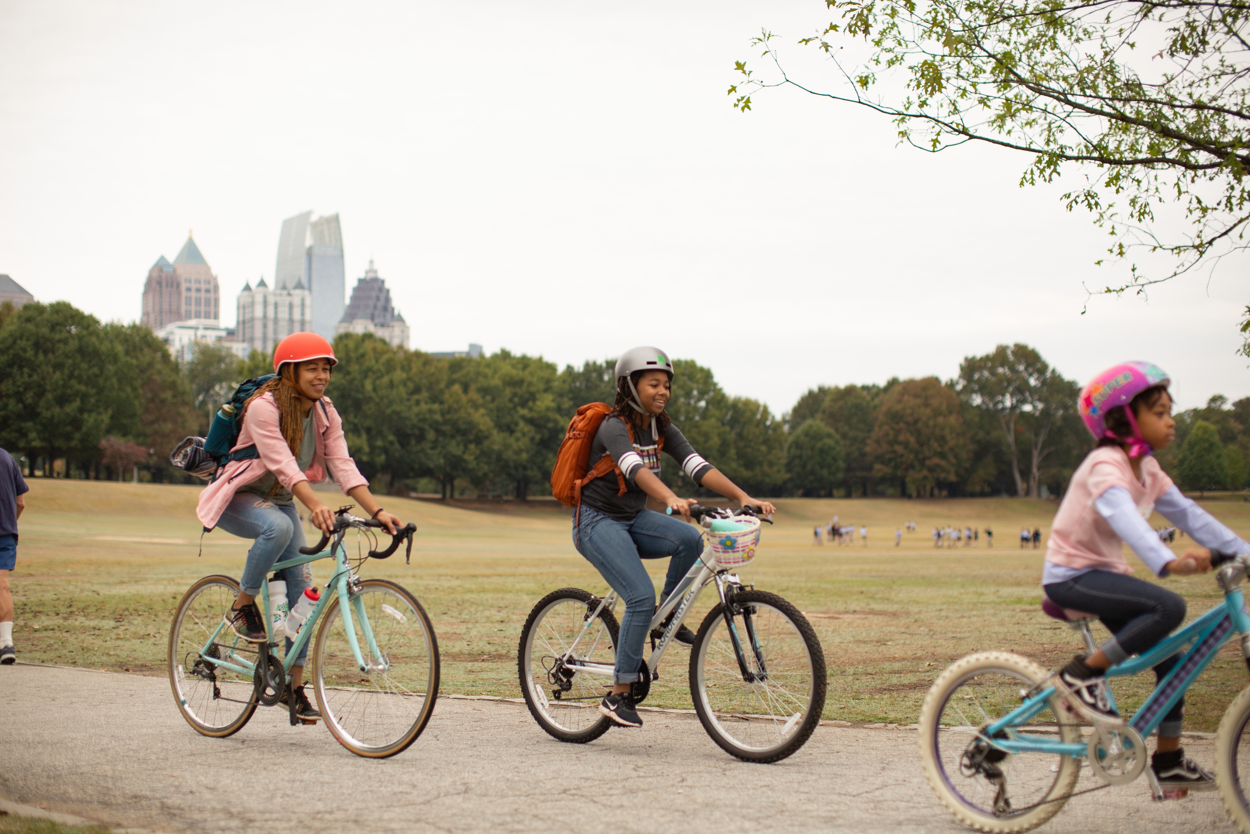 Three youth ride bikes on a path through a park. 