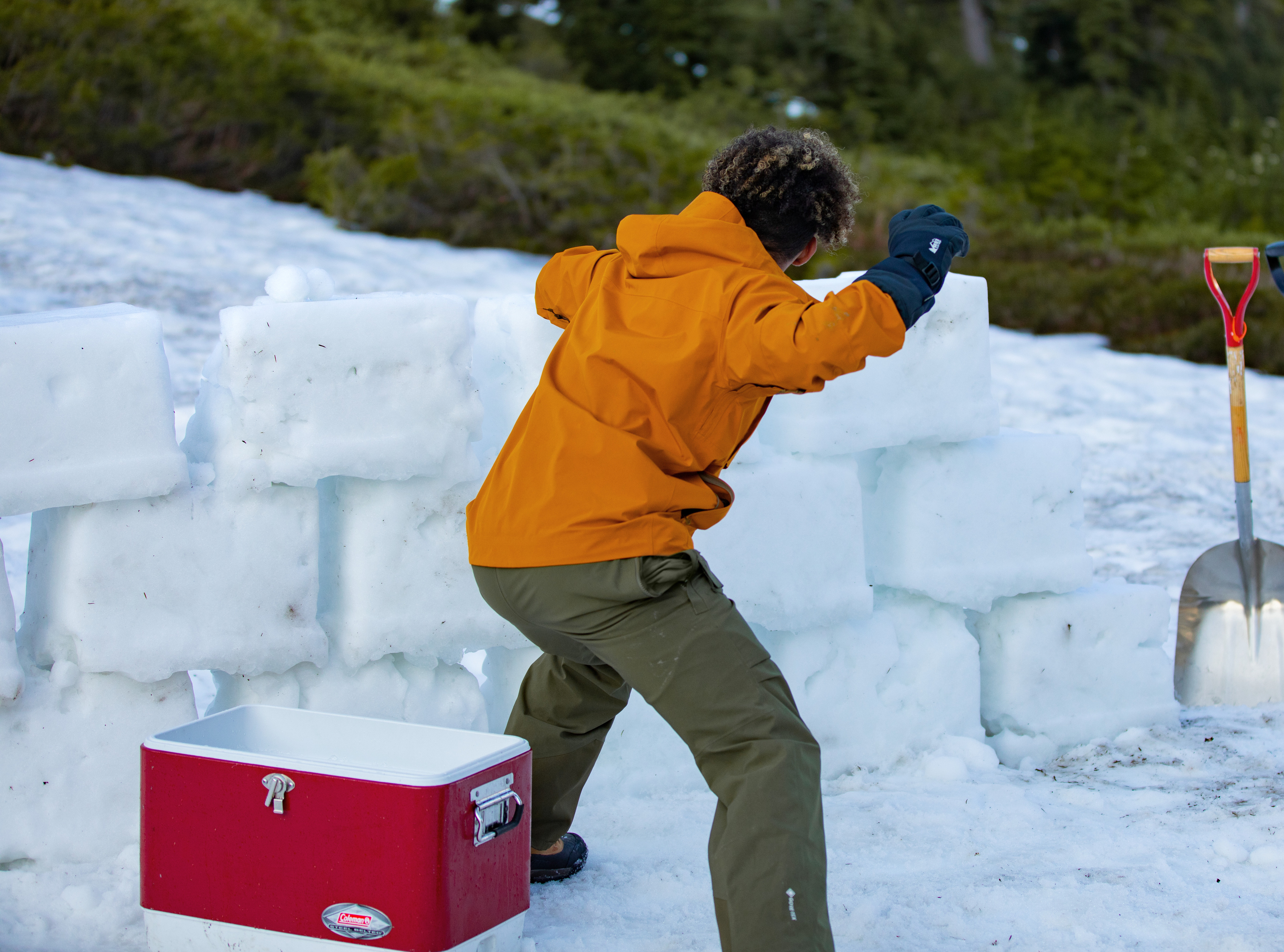 A kid plays behind an extensive snow brick wall while throwing snowballs from his cooler