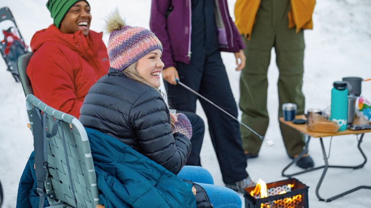 Campers roast marshmallows around a campfire in the snow.