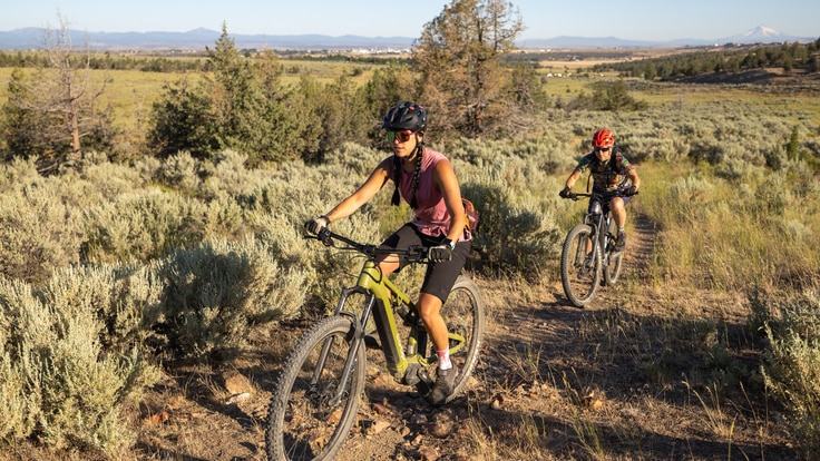 Two mountain bike riders cruise a dirt path using an electric mountain bike