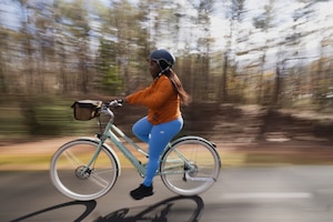 Woman cycling wearing blue leggings, an orange long sleeve shirt and a navy blue helmet