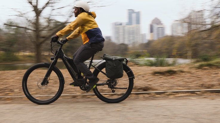 A person riding an electric bike past an urban skyline.