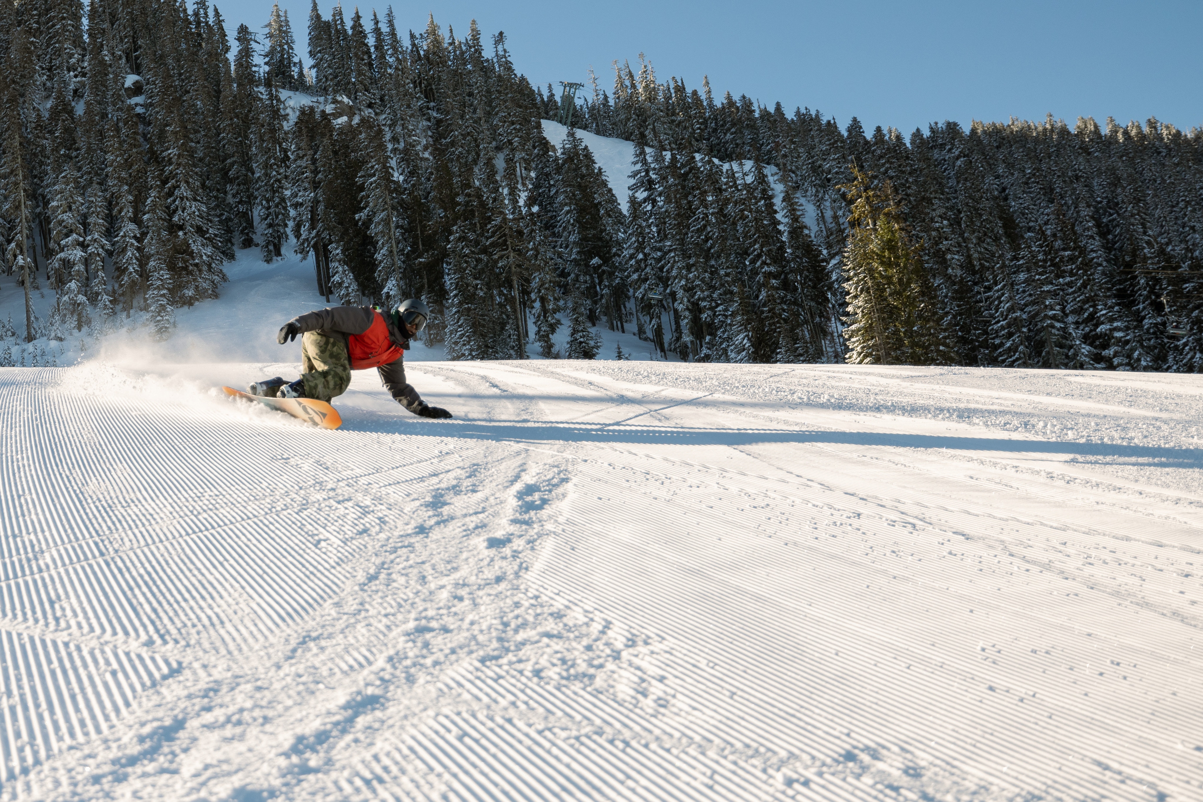 Snowboarder turns down a groomed mountain run