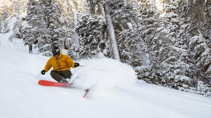 A skier shreds down a mountain in a bright yellow jacket