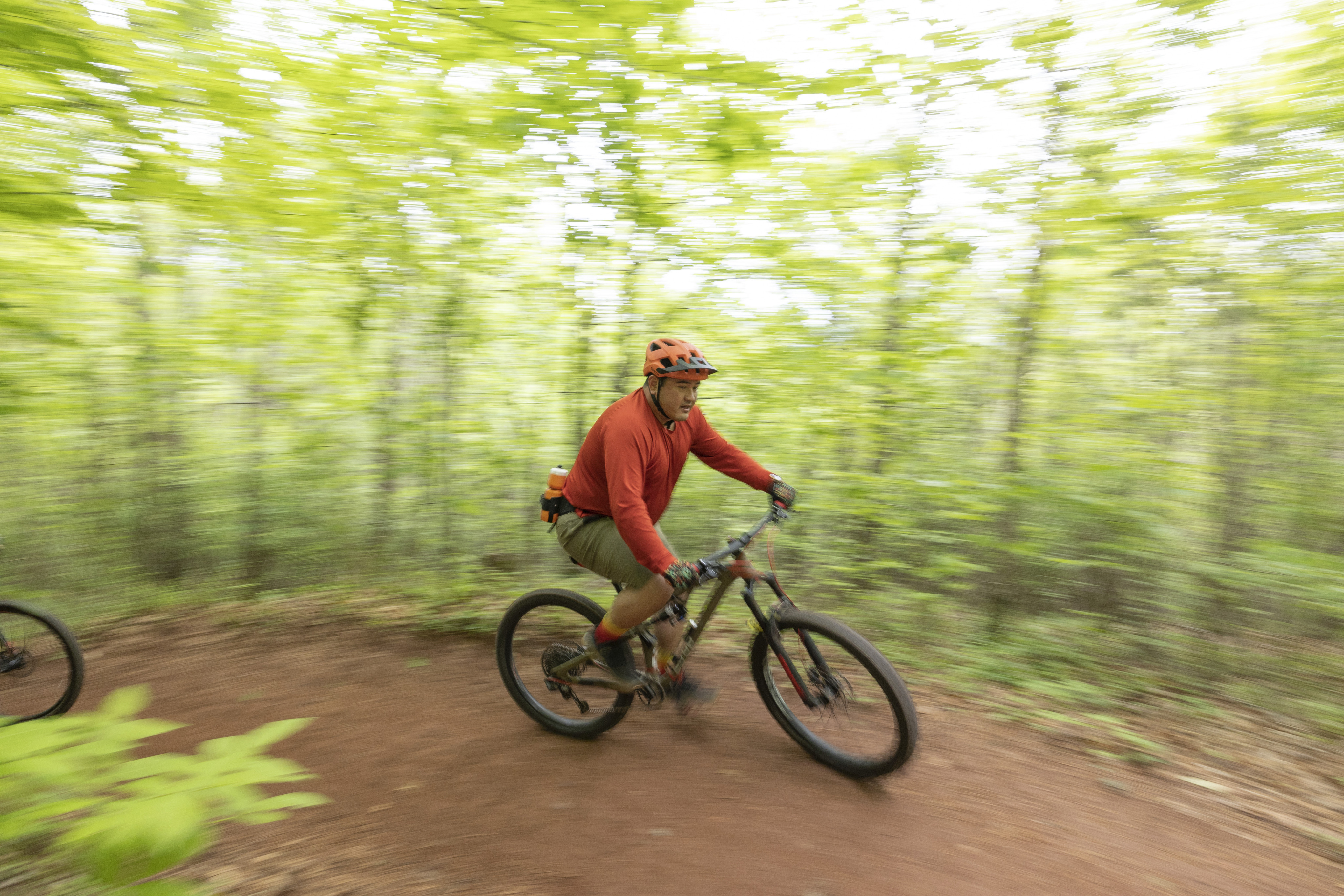 Mountain biker takes a curve wearing a bright orange shirt and helmet