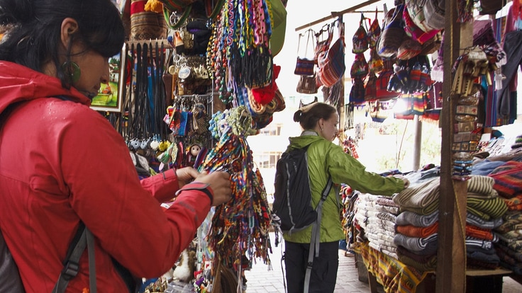 Two travelers looking at blankets and bracelets at an outdoor market.