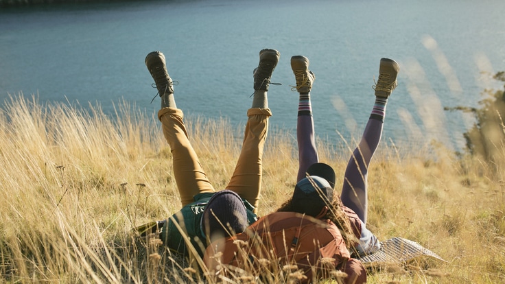 Two people laying on their backs in a field with their feet in the air.