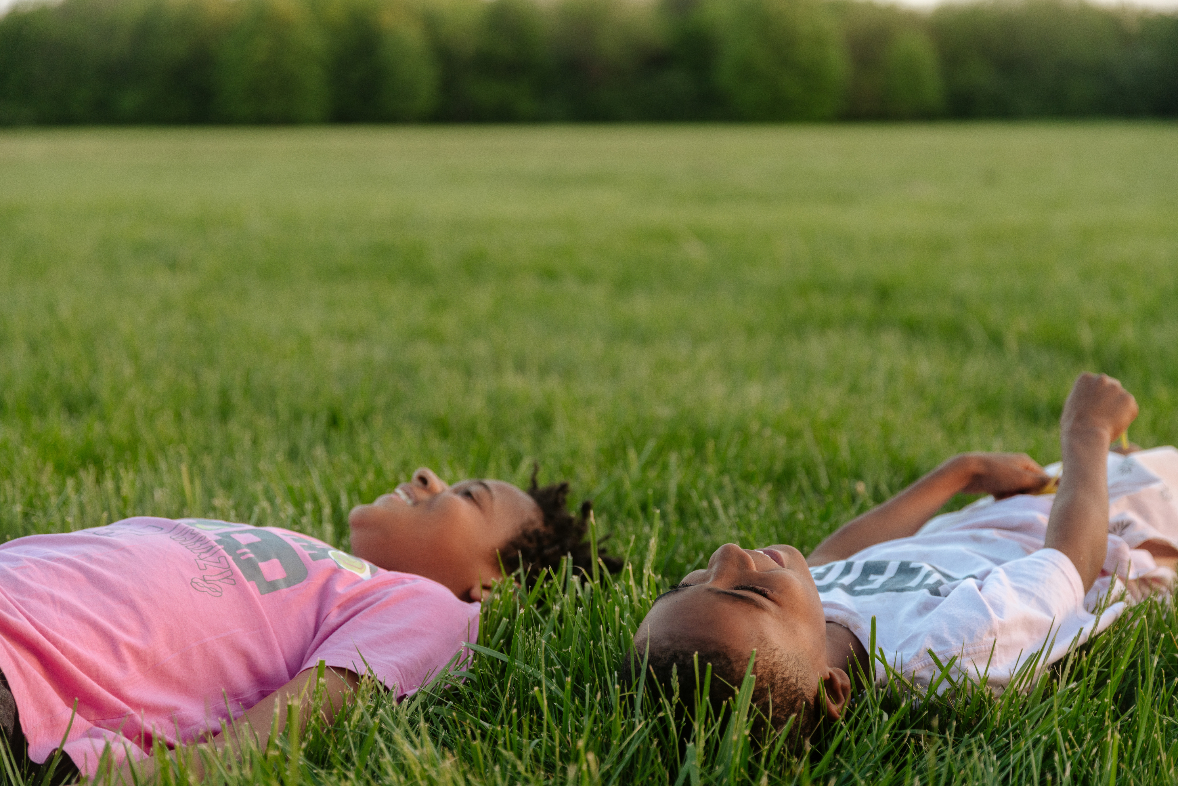 Two children lay in a field of green grass, enjoying time outside in nature