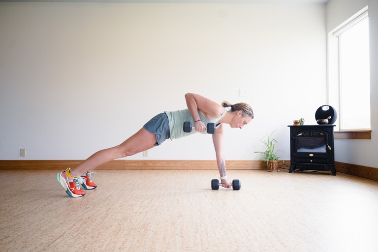 A woman performs plank row with dumbbells in each hand