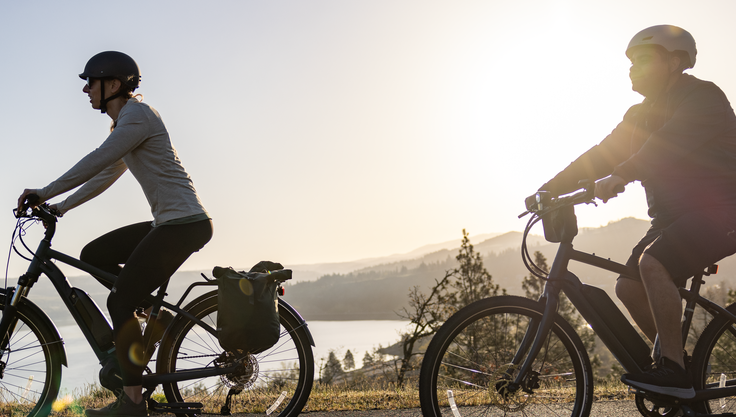 Two people riding e-bikes along a path