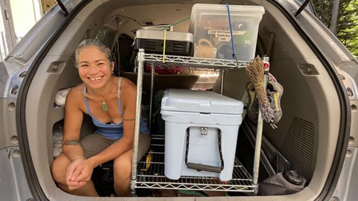 Chef Maria Hines sits in the back of her vehicle near a cooler.